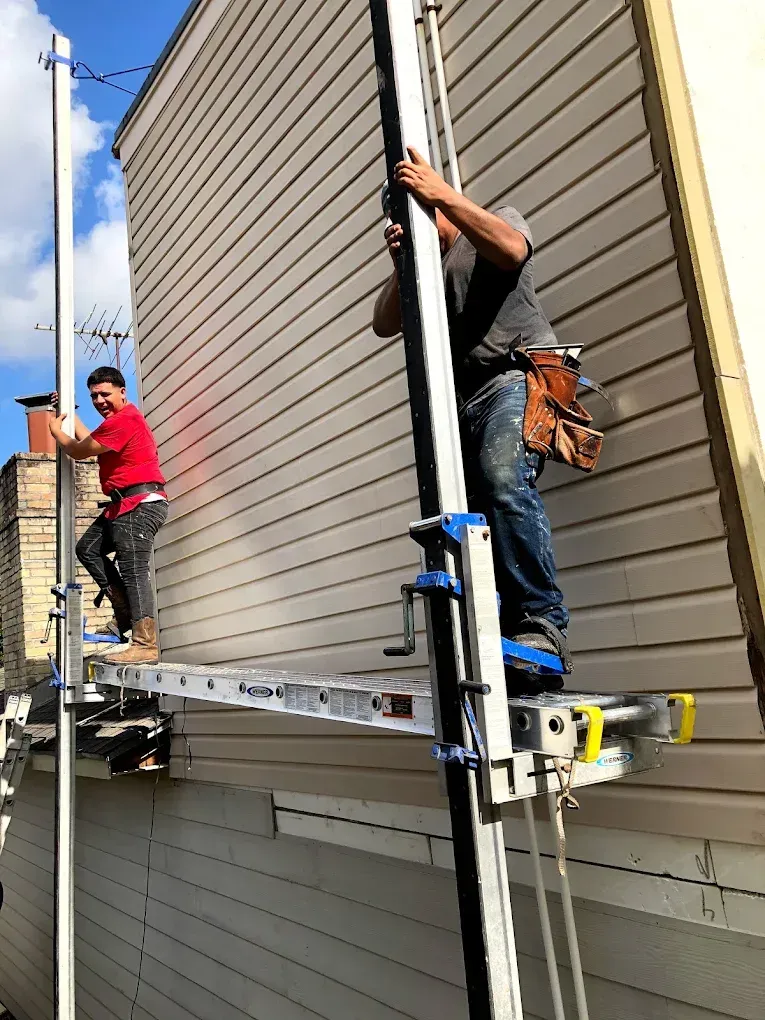 Two construction workers on a scaffolding platform by a building.