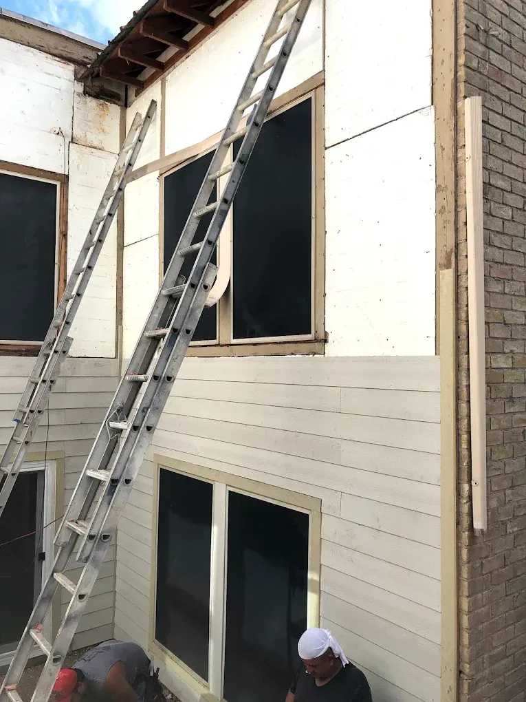 Exterior house undergoing renovation; workers install siding and frame windows.