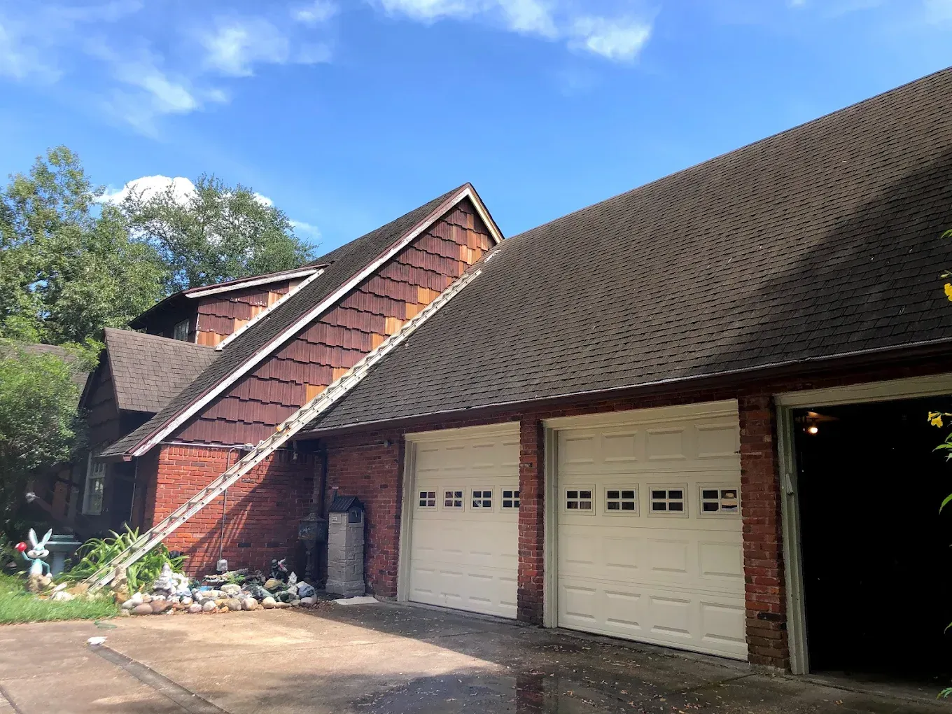 A brick house with brown shingled roof and two garage doors. A ladder leans against the side.