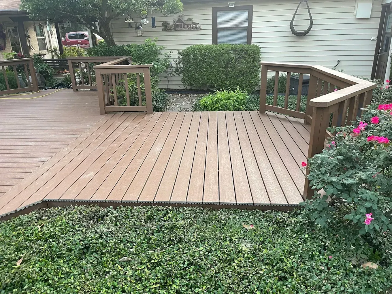 Wooden deck with railings, brown wood, and surrounding green bushes.