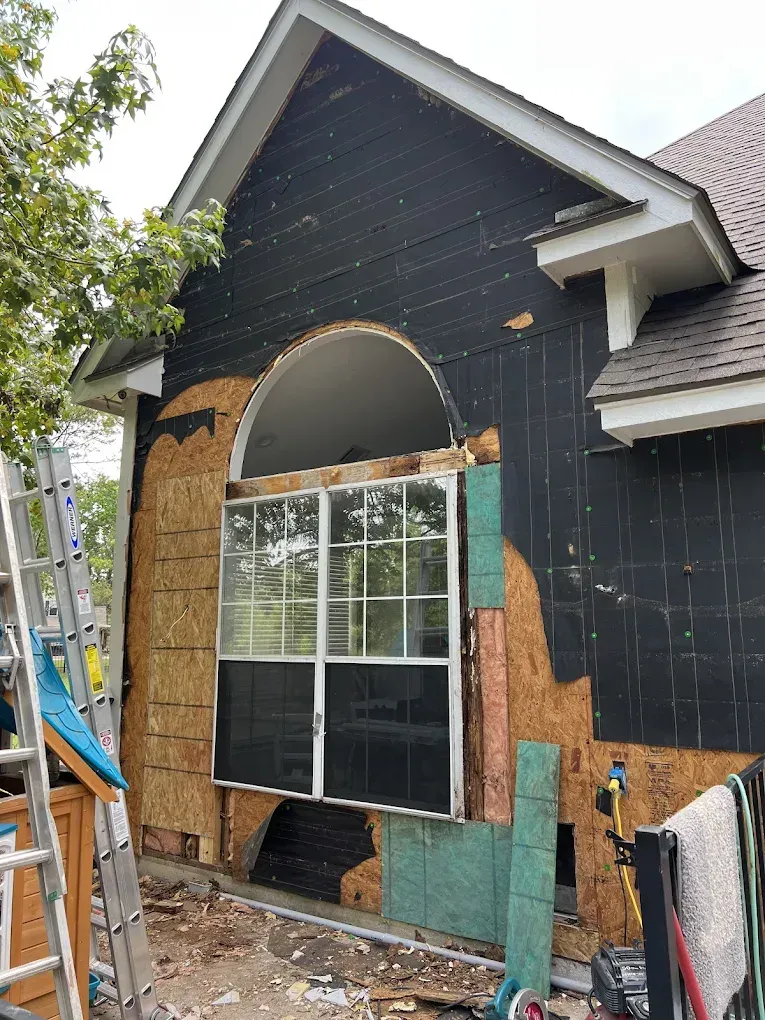 Exterior wall of a house with a window partially removed. Black siding is visible.