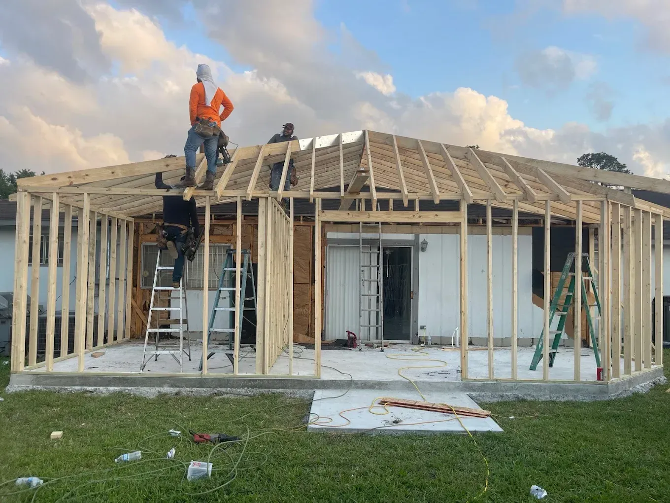 Construction workers framing a new structure onto the back of a house, working on a roof.