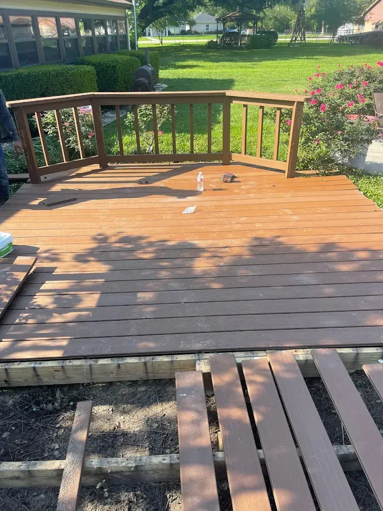 Wooden deck being renovated; some boards removed. Brown deck with a brown railing, overlooking grass.