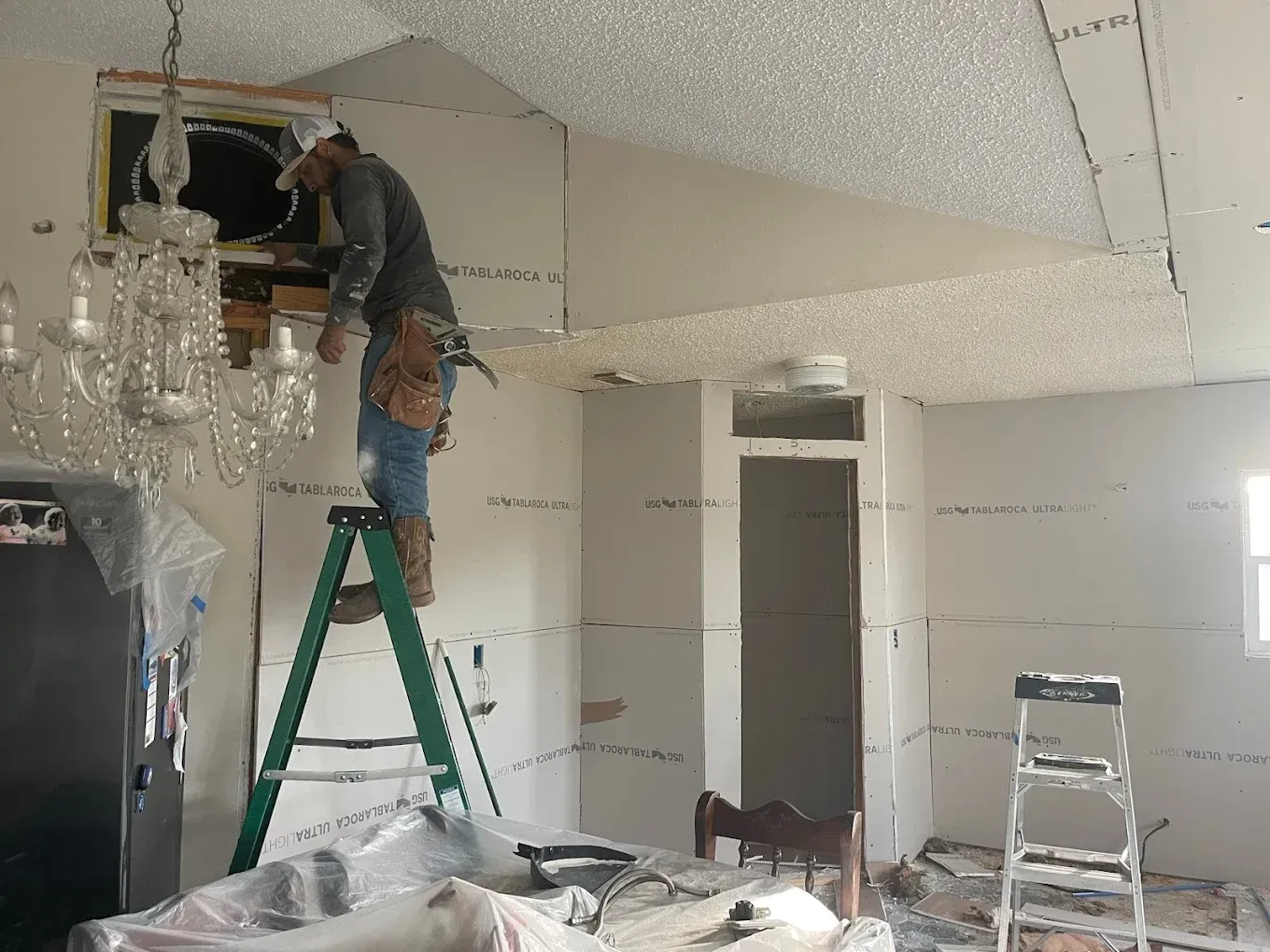 A construction worker installing drywall in a room with a chandelier