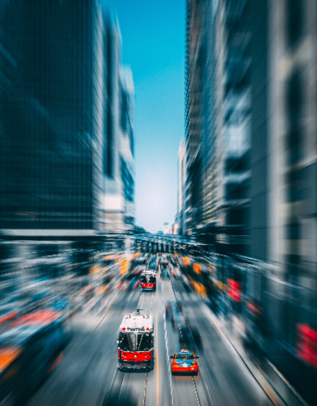 Street-level view of a city with tall buildings on either side, a red streetcar and cars moving down the street.