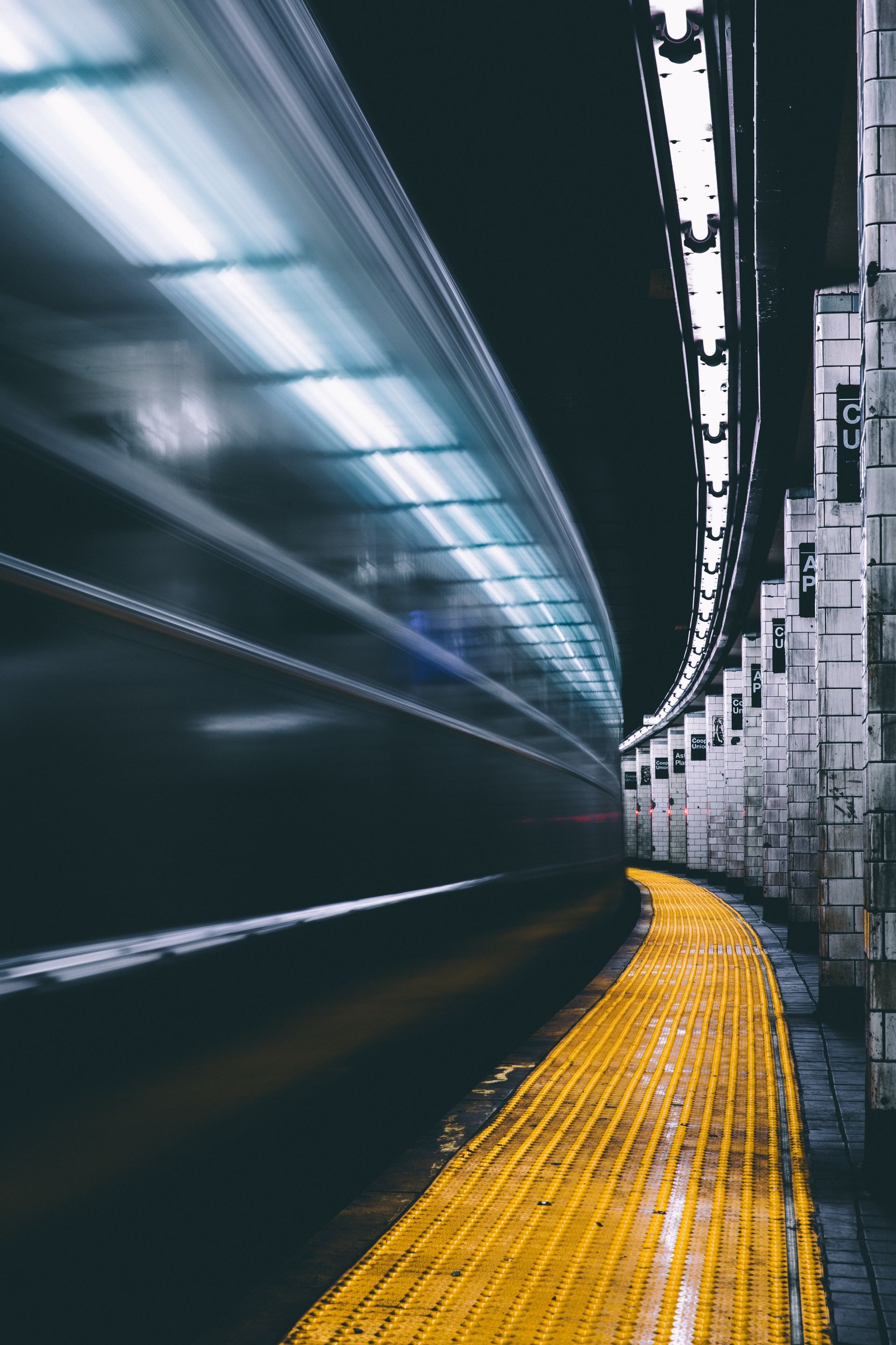 A speeding subway train blurred in a dark, curved tunnel, with a yellow platform strip on the right.