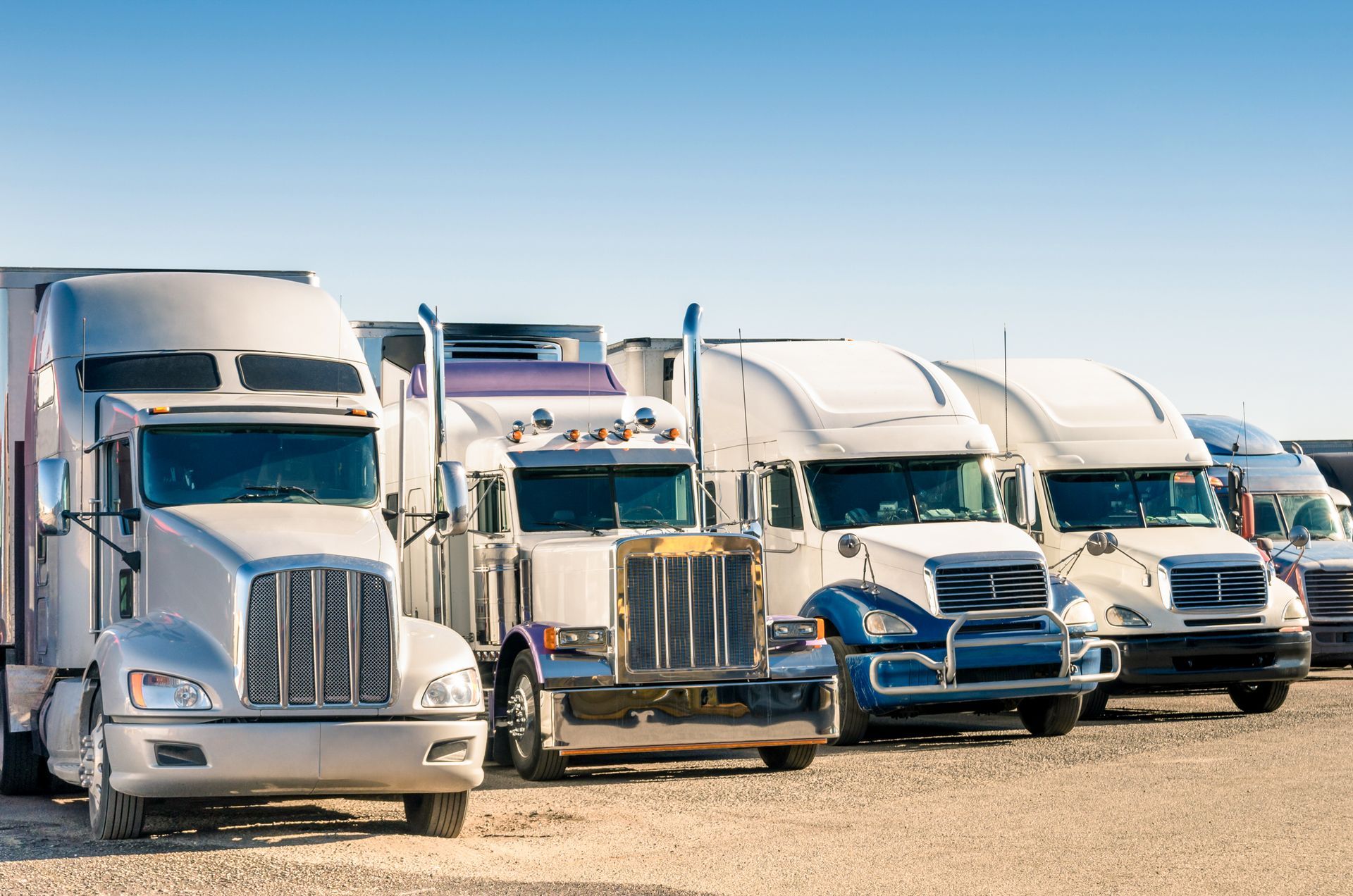 a row of semi trucks are parked in a dirt lot .