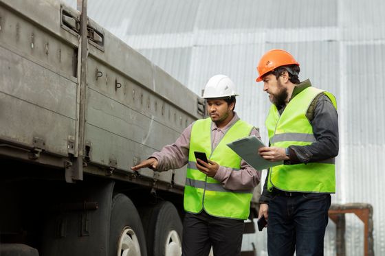 two men are standing next to a truck looking at a tablet .