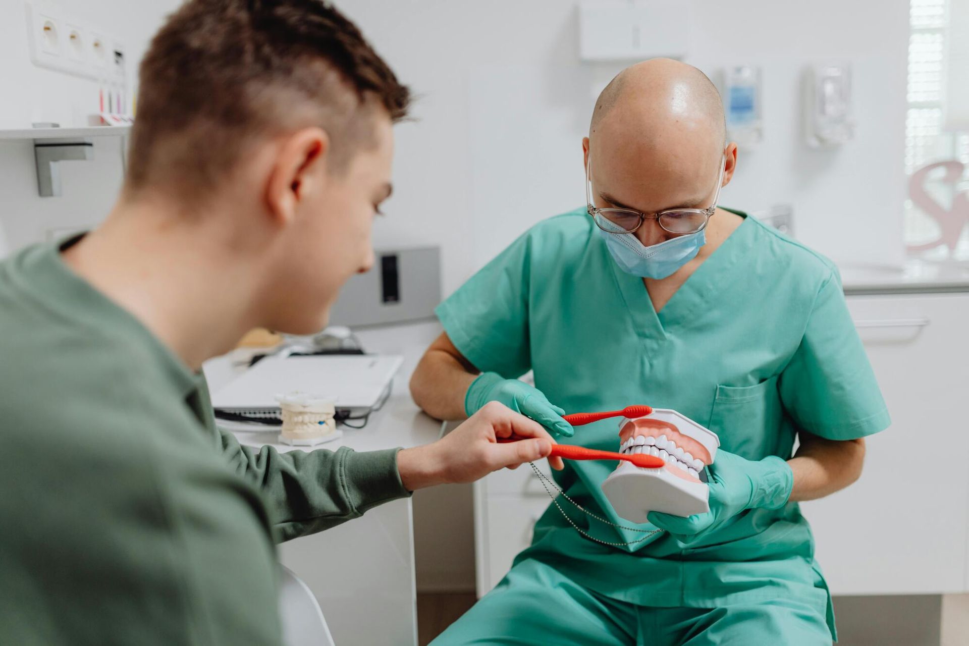 A dentist is brushing a patient 's teeth with a model of teeth.