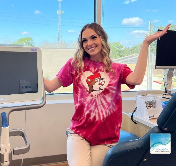 A woman in a red tie dye shirt is sitting in a dental chair.