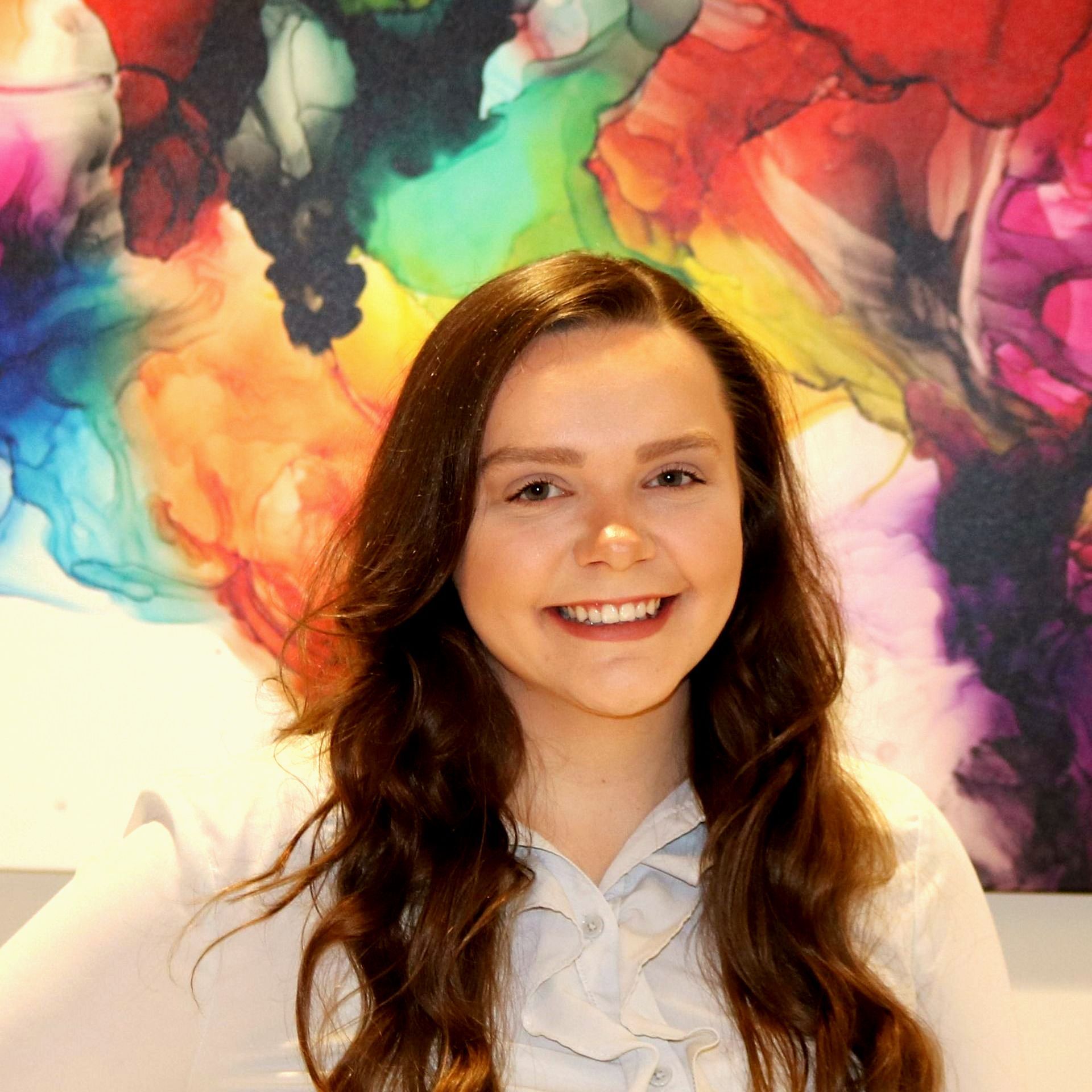 A woman is smiling in front of a colorful painting.