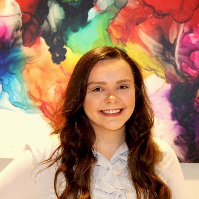 A woman is smiling in front of a colorful painting.