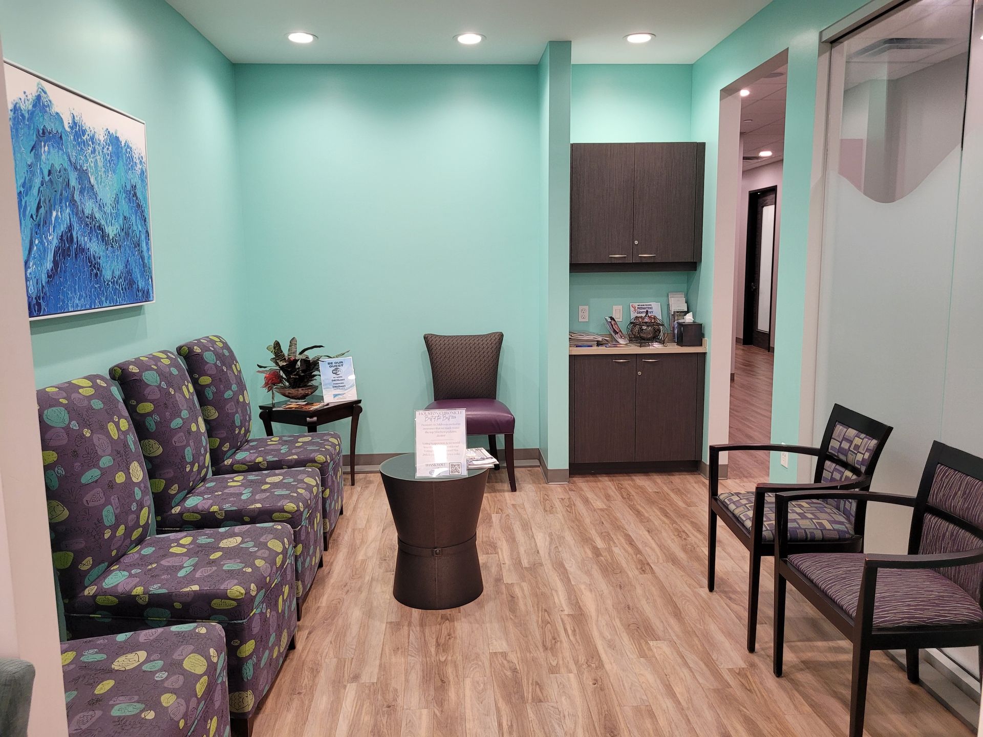 A waiting room with chairs , a table and a painting on the wall.