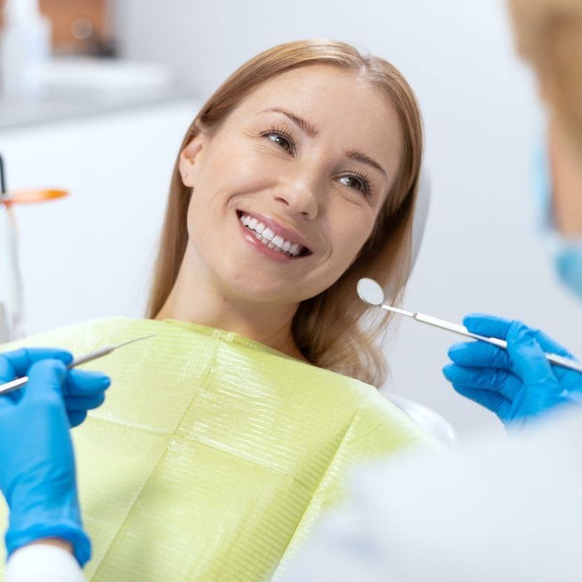 A woman is smiling while having her teeth examined by a dentist.