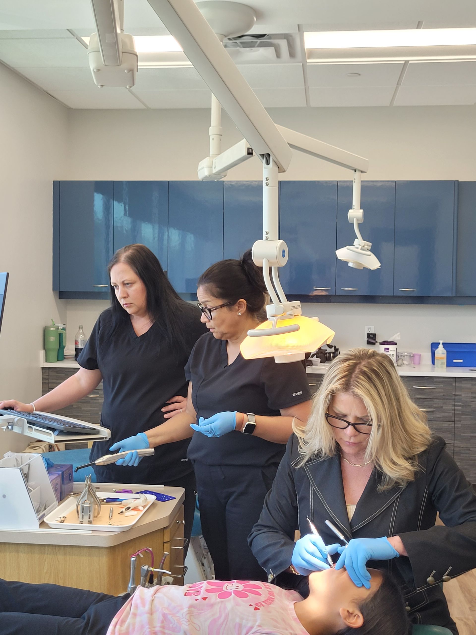 A group of women are working on a child 's teeth in a dental office.