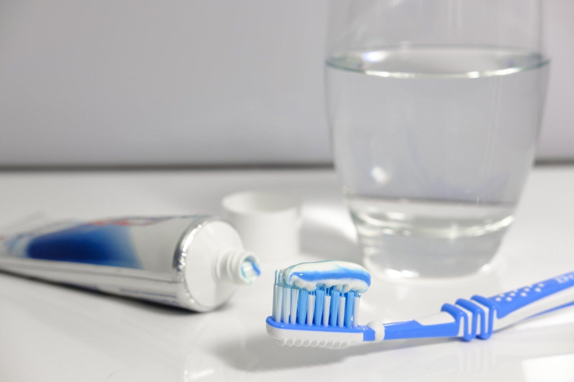 A toothbrush with toothpaste on it next to a tube of toothpaste and a glass of water.