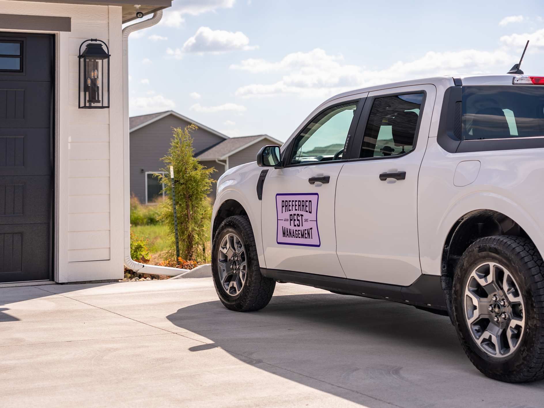 White pickup truck parked in driveway next to a garage; sign on truck door.