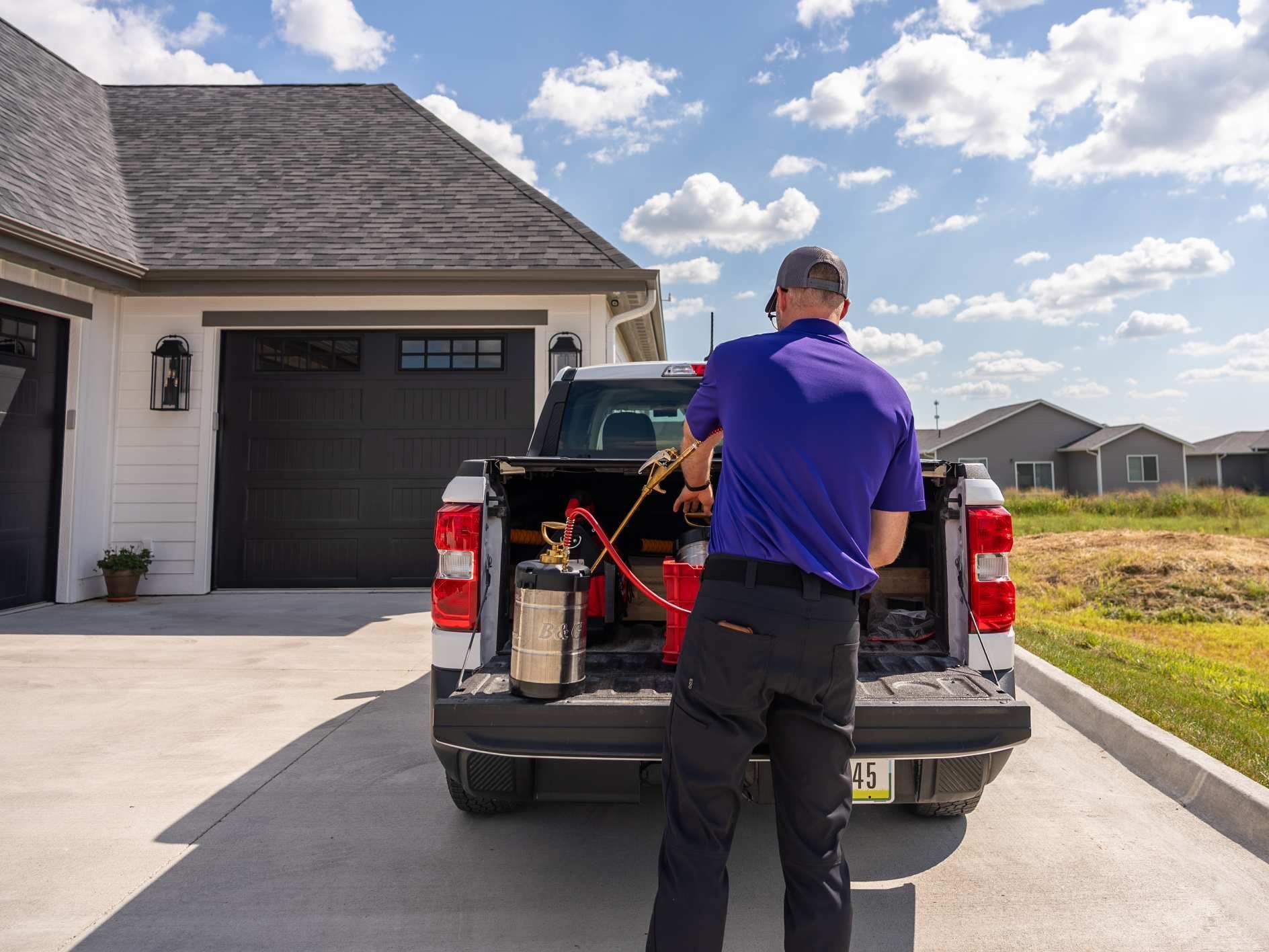Man in purple shirt removing equipment from a truck in front of a house.