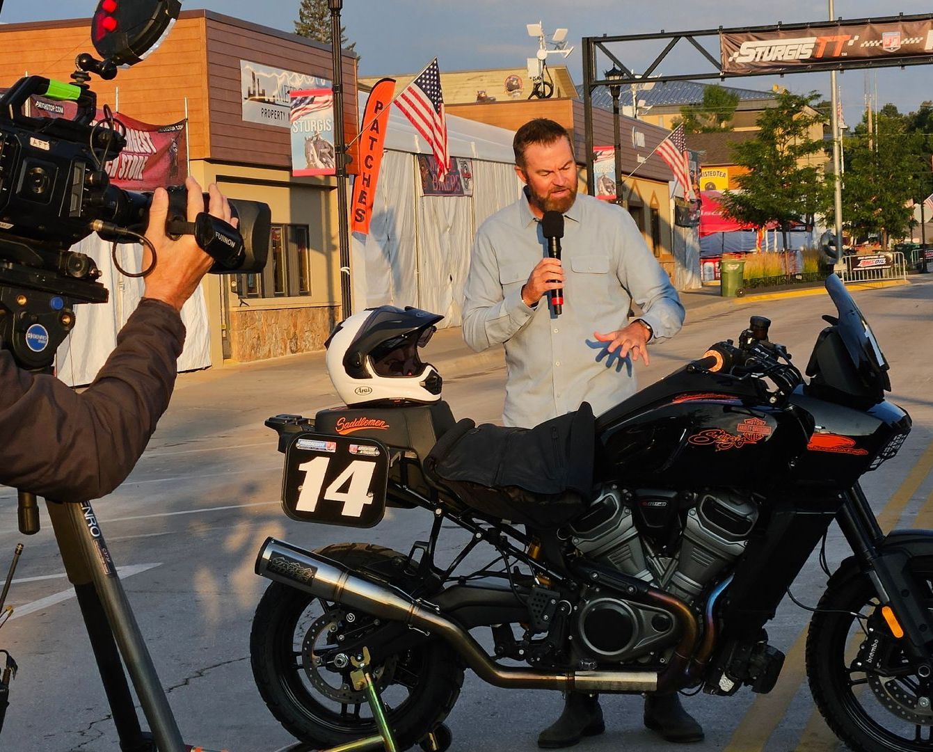 A man is talking into a microphone next to a motorcycle with the number 14 on it