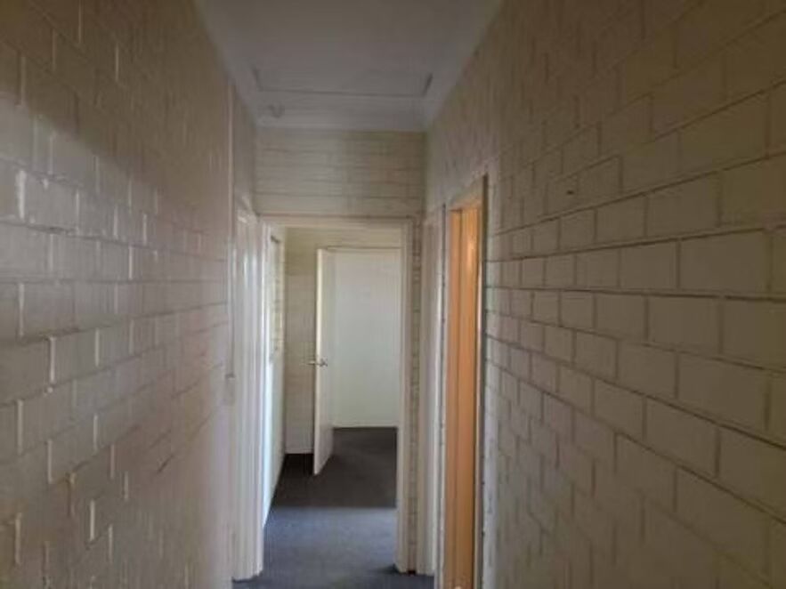 A long hallway with white brick walls and a door leading to a room.
