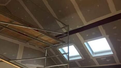 A scaffolding is sitting under a ceiling with two skylights.