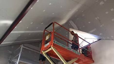 A man is standing on a scissor lift working on a ceiling.