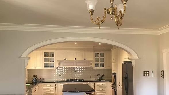 A kitchen with white cabinets and black counter tops and a chandelier hanging from the ceiling.