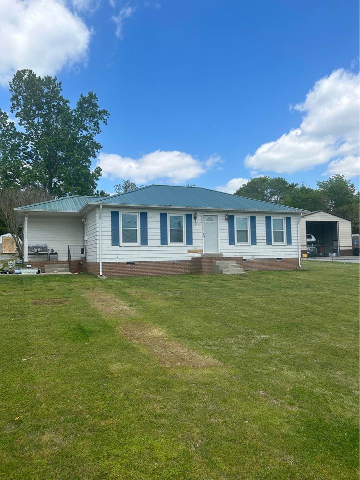 A white house with a blue roof is sitting on top of a lush green field.