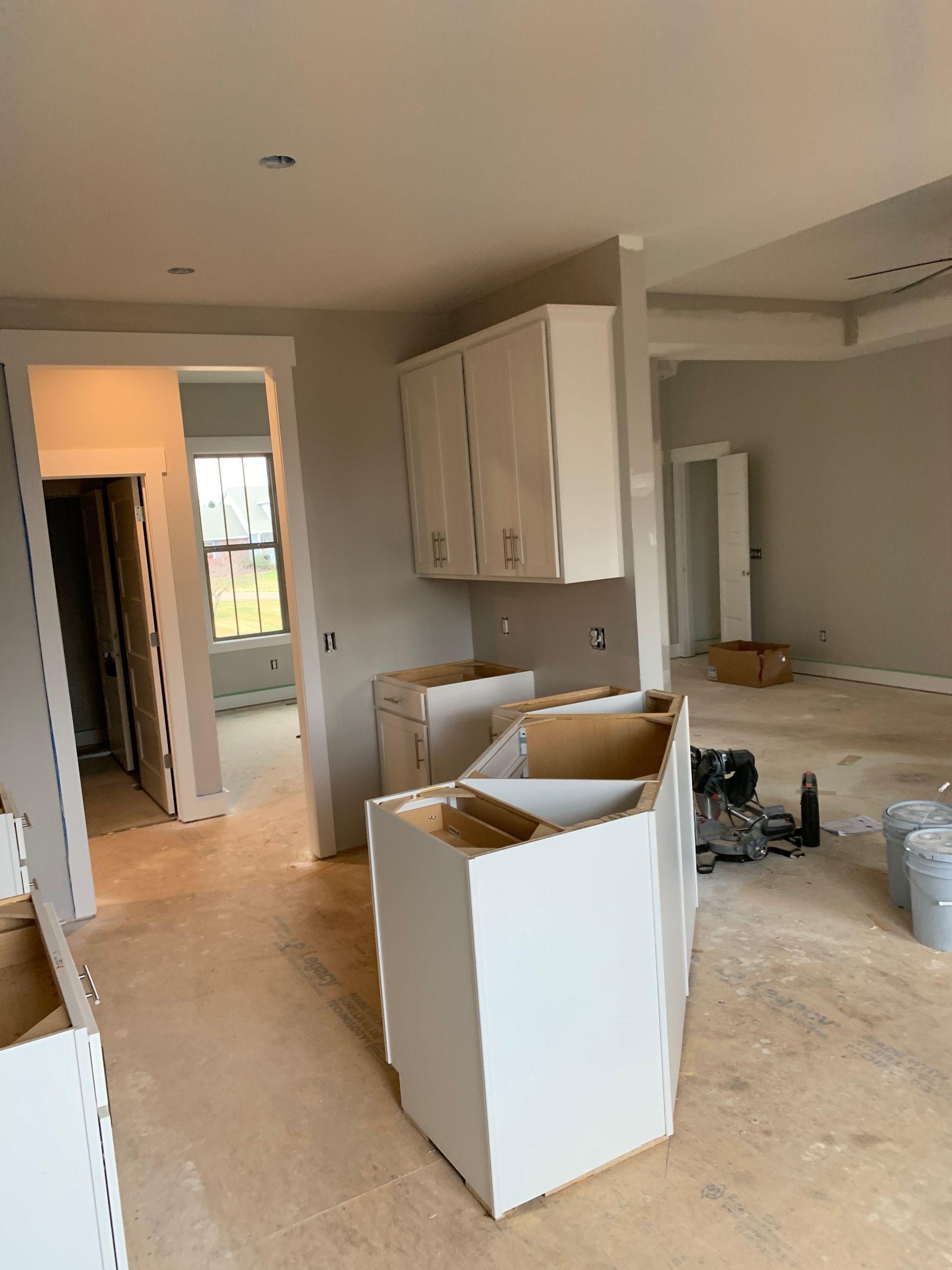 A kitchen under construction with white cabinets and a wooden floor.