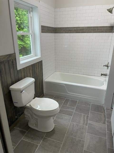 A bathroom with a toilet , tub , shower and window.
