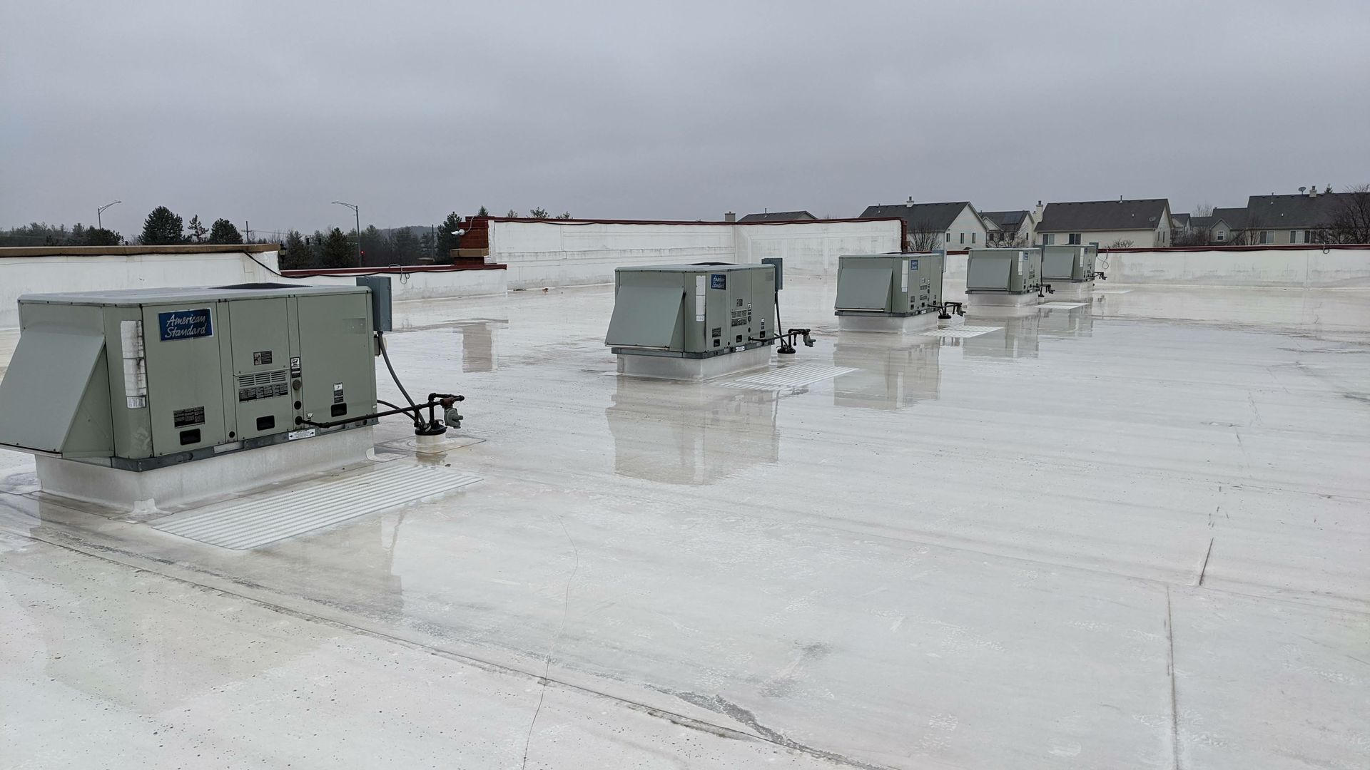 Rooftop with several gray HVAC units on a white flat roof under an overcast sky.