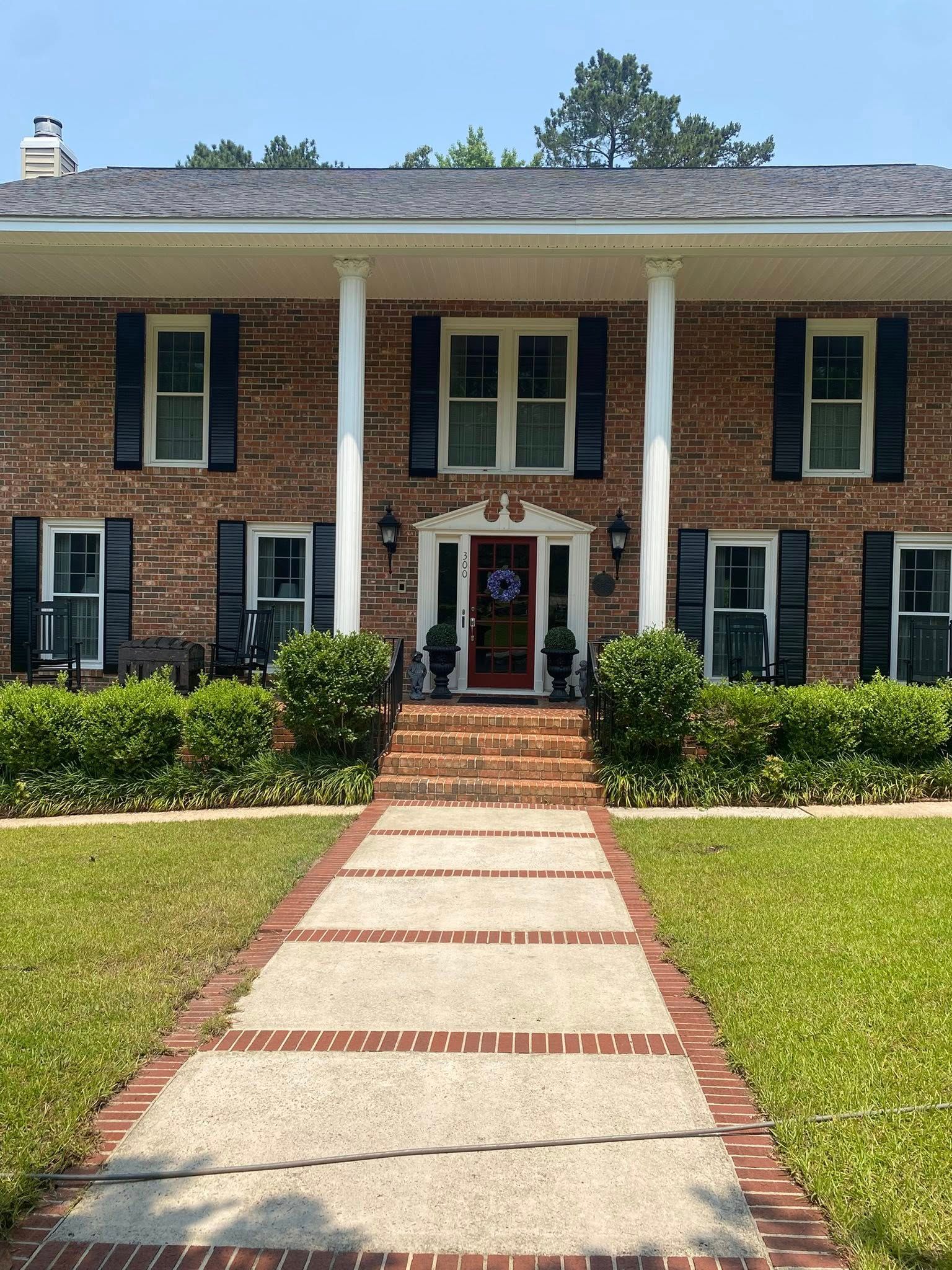Two-story brick house with white columns and a red-brick walkway leading to the front door.