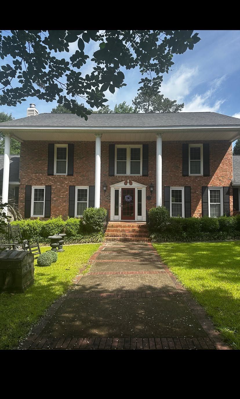Brick two-story house with white columns, front walkway, and green lawn under leafy trees