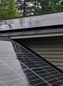 Solar panels on a house roof beneath trees, with one panel partially detached at the edge.