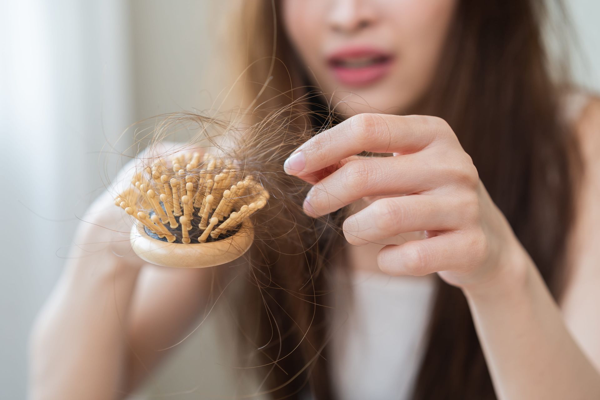 Hairbrush with tangled hair strands while a woman holds a loose strand near it