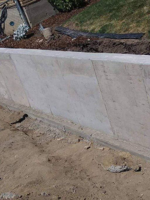 Concrete retaining wall bordering brown soil and green grass.