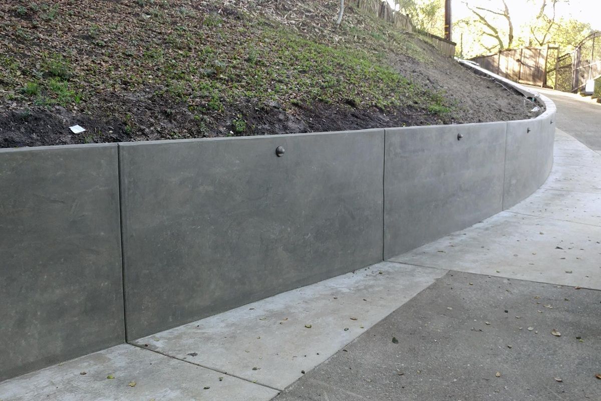 Concrete retaining wall curving alongside a pathway, supporting a grassy hill.