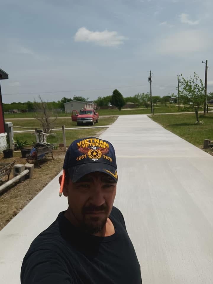 Man wearing a "Vietnam Veteran" hat in front of a new concrete driveway with a red truck in the distance.