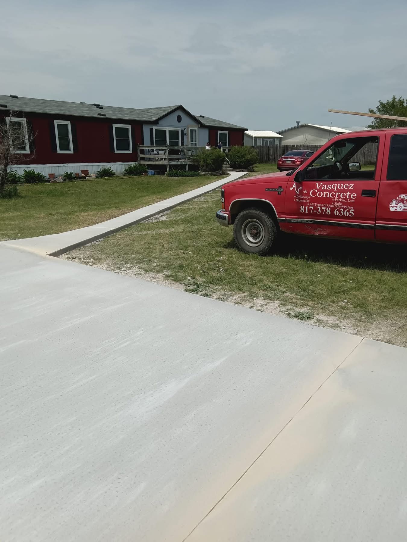 Red pickup truck parked on grass next to a newly poured concrete driveway and walkway in front of a house.