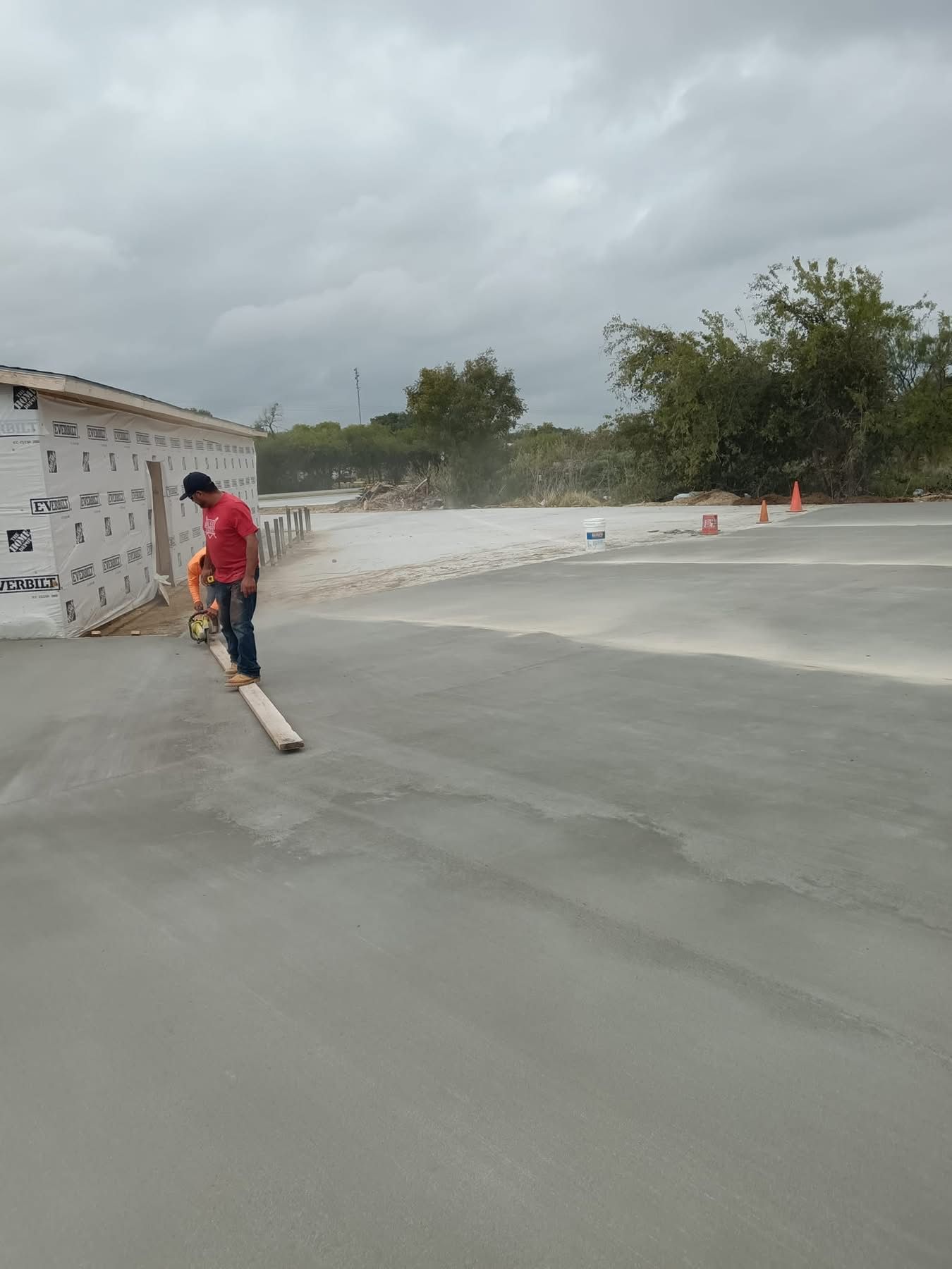 Person smoothing concrete with a tool. Exterior shot. Gray cement and cloudy sky.