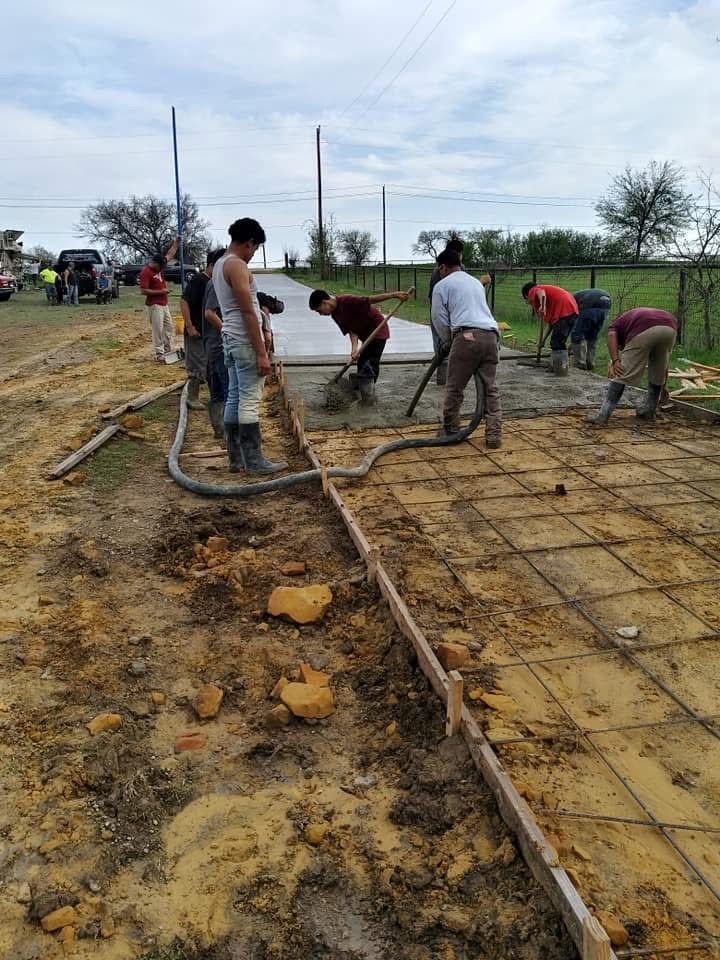 Group of people pouring concrete for a path. They are using tools and working on a dirt ground.