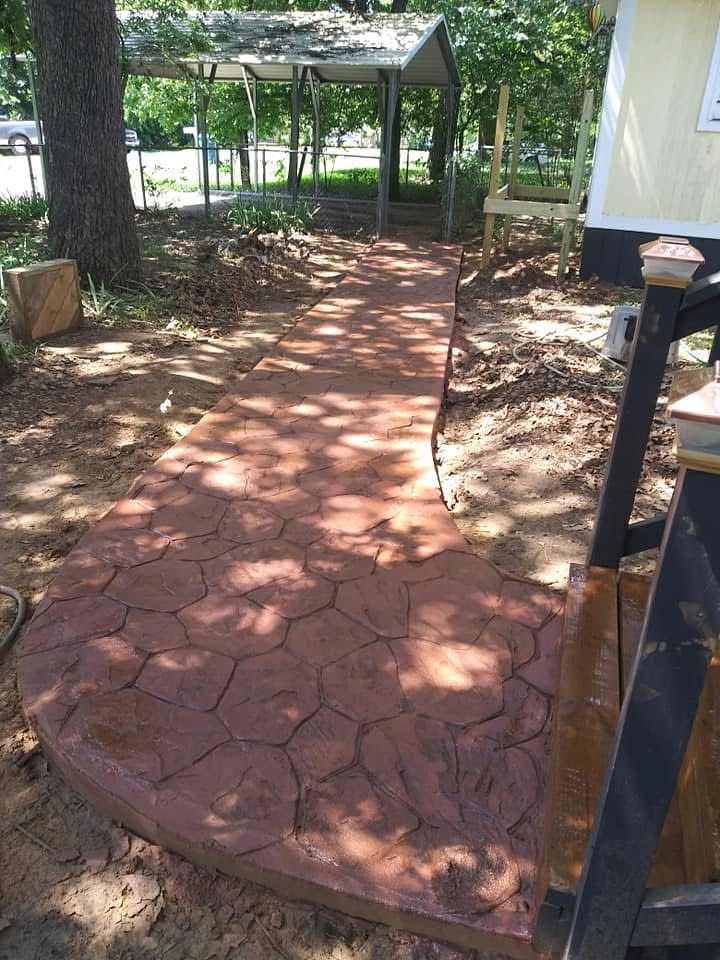 Red, textured concrete walkway leading to a gazebo, in an outdoor setting.