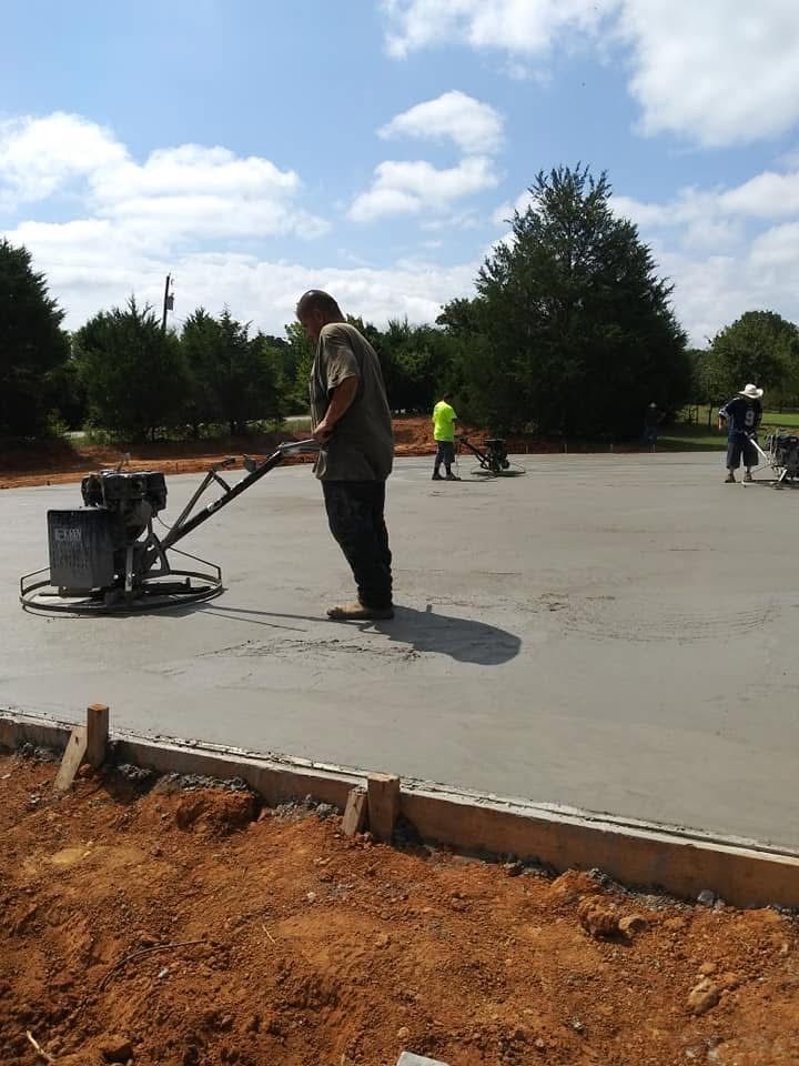Construction workers using power trowels to finish a concrete slab on a sunny day.