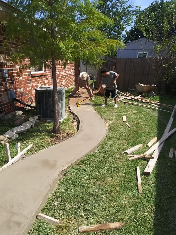 Two people laying a curved concrete walkway in a backyard; one is smoothing the concrete.
