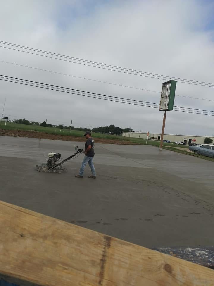 Person using a concrete finishing machine on a newly poured concrete surface, outdoors near a sign and power lines.