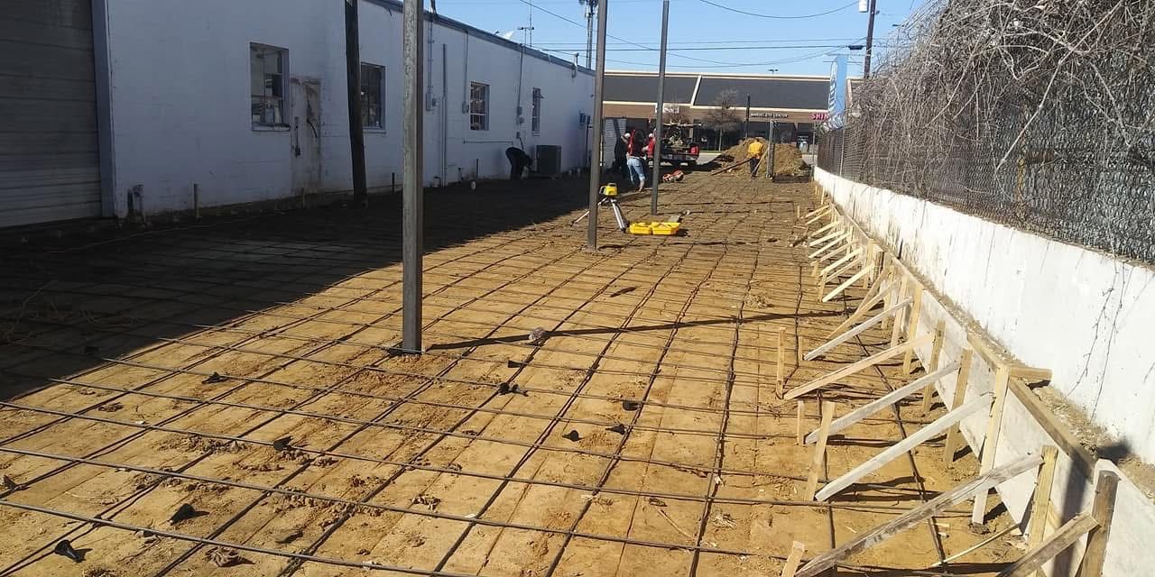 Construction site: rebar grid laid on dirt, with forms for a concrete wall along a fence.