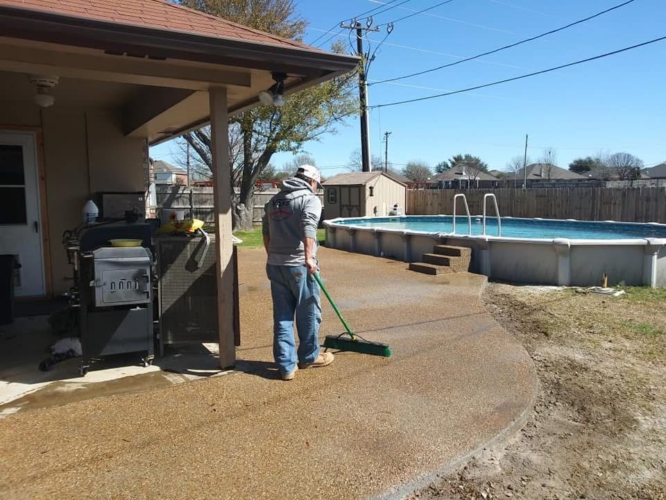 Person sweeping a concrete patio next to a pool.
