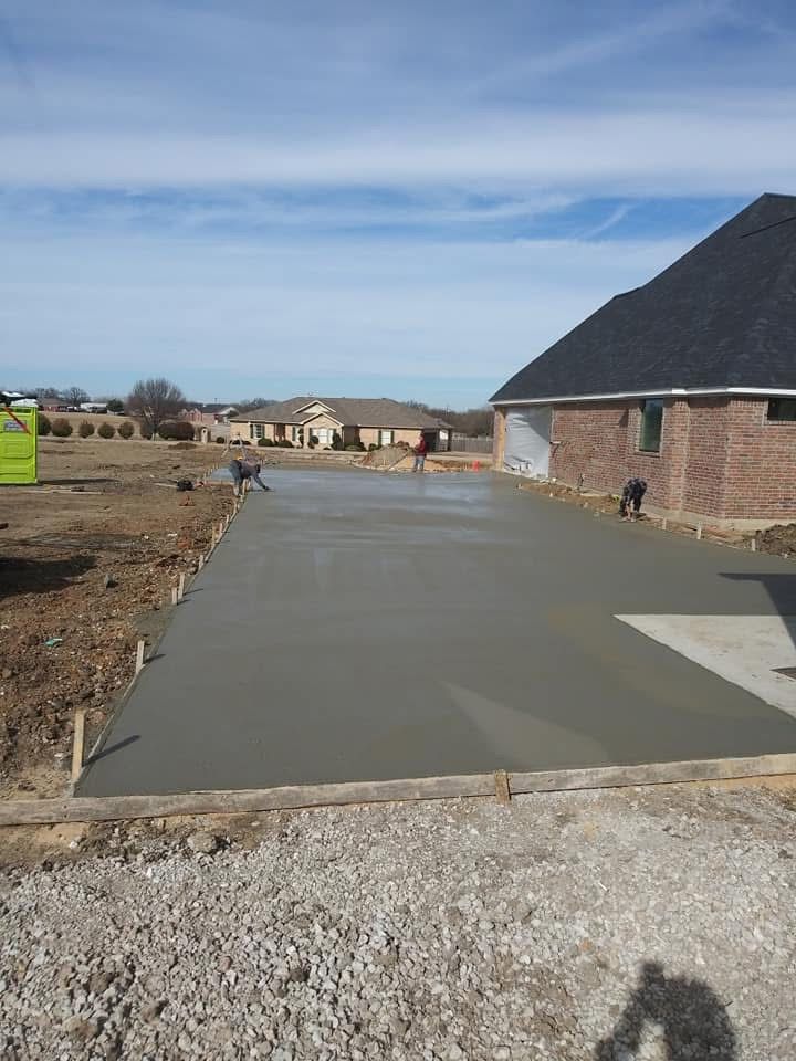 Freshly poured concrete driveway next to a brick building under a blue sky.