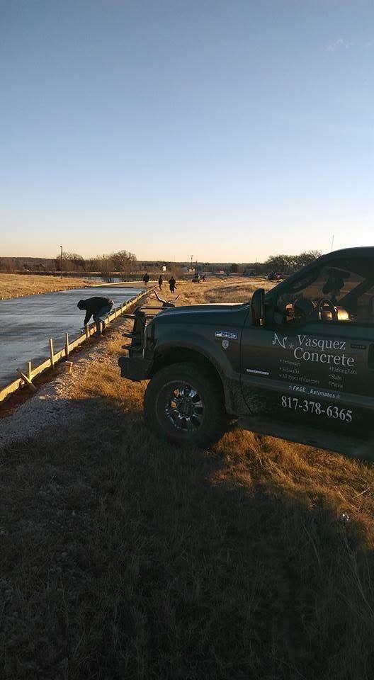 Construction workers pouring concrete; a truck with business logo parked. Sunny, outdoor setting.