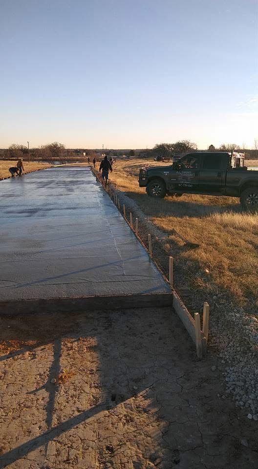 Construction workers pouring concrete for a driveway, with a truck nearby on a sunny day.